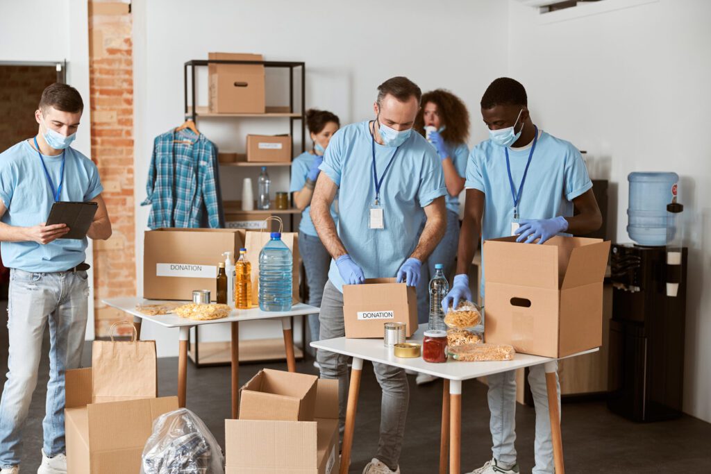 Packing Services in Glendale Full length shot of diverse volunteers in blue uniform, protective masks and gloves separating donations stuffs, sorting items in cardboard boxes while standing indoors