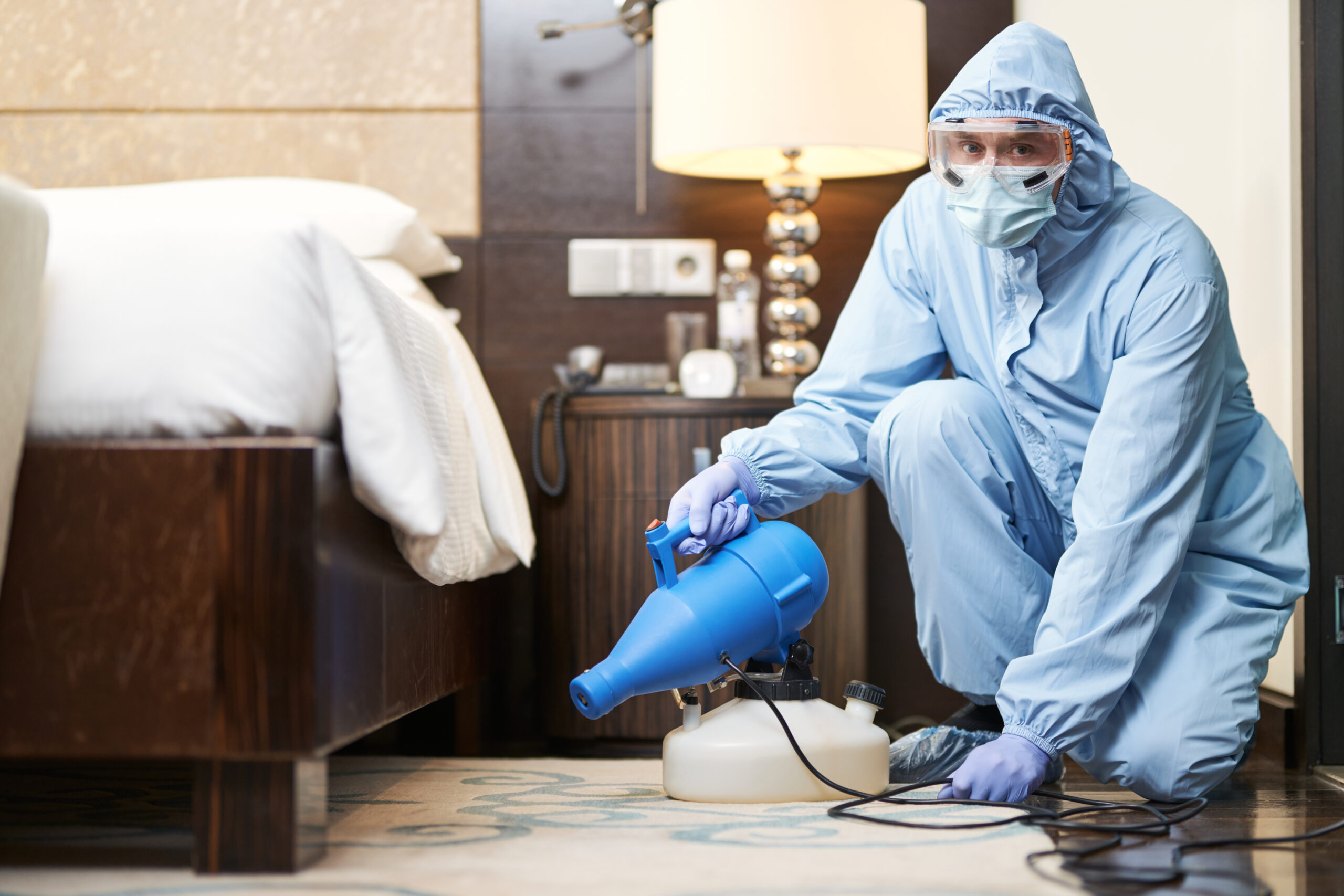 Bed Bug Control Services Oak Hills CA Full length shot of two professional plumbers, workers in uniform fixing or installing heating radiator. Construction, maintenance and repair concept. Worker in biohazard suit and mask disinfecting bedroom