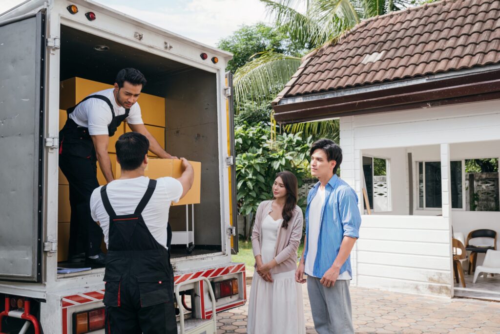 Professional Movers in Yonkers, NY Employees work in unison to help a couple relocate to their new home. They efficiently unload and lift cardboard boxes providing top-notch delivery service. Moving Day Concept