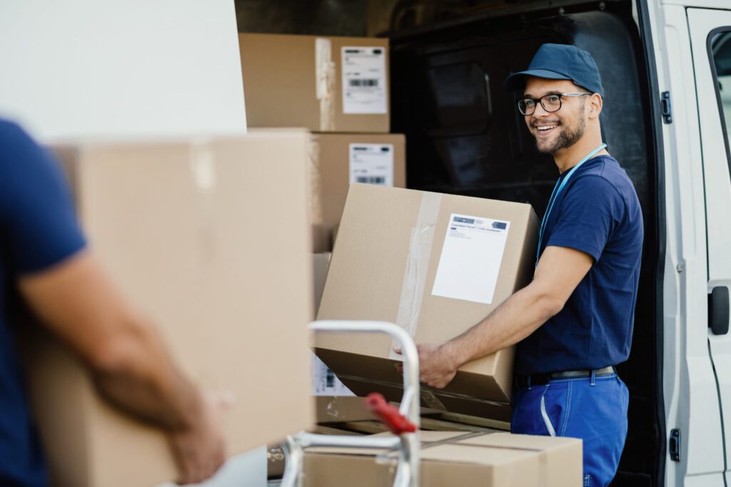 Commercial Moving Services in Hartford, CT Happy delivery man talking with coworker while loading boxes in a truck.