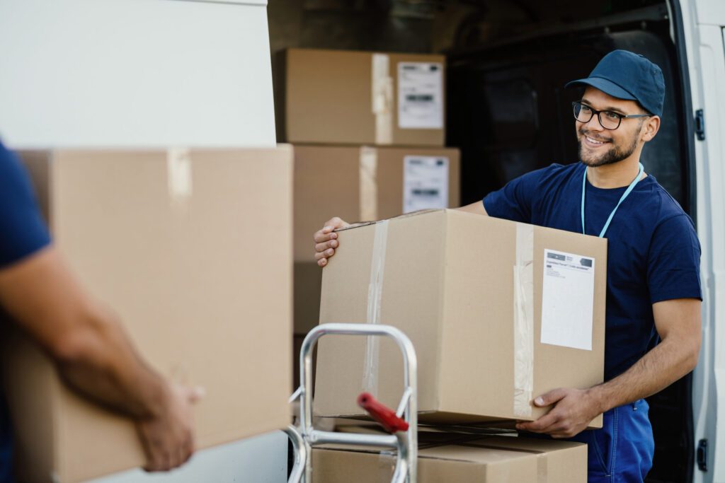 Long Distance Movers in New York City NY Happy manual worker unloading cardboard boxes from delivery van.