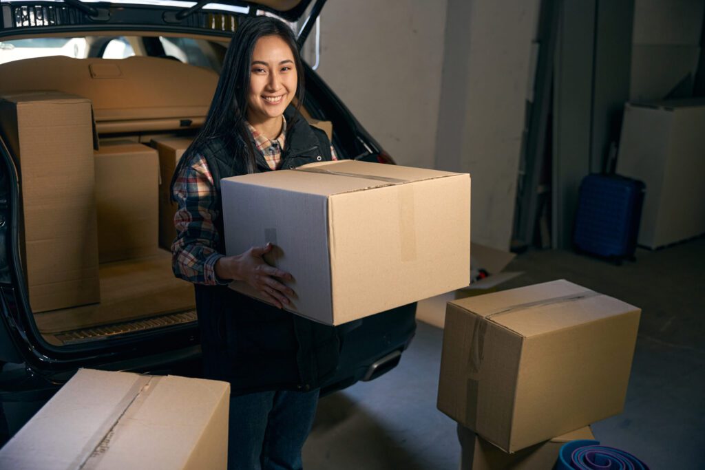 Affordable Home Movers Happy woman sitting in the trunk of a car with a box in her hands. Cropped photo