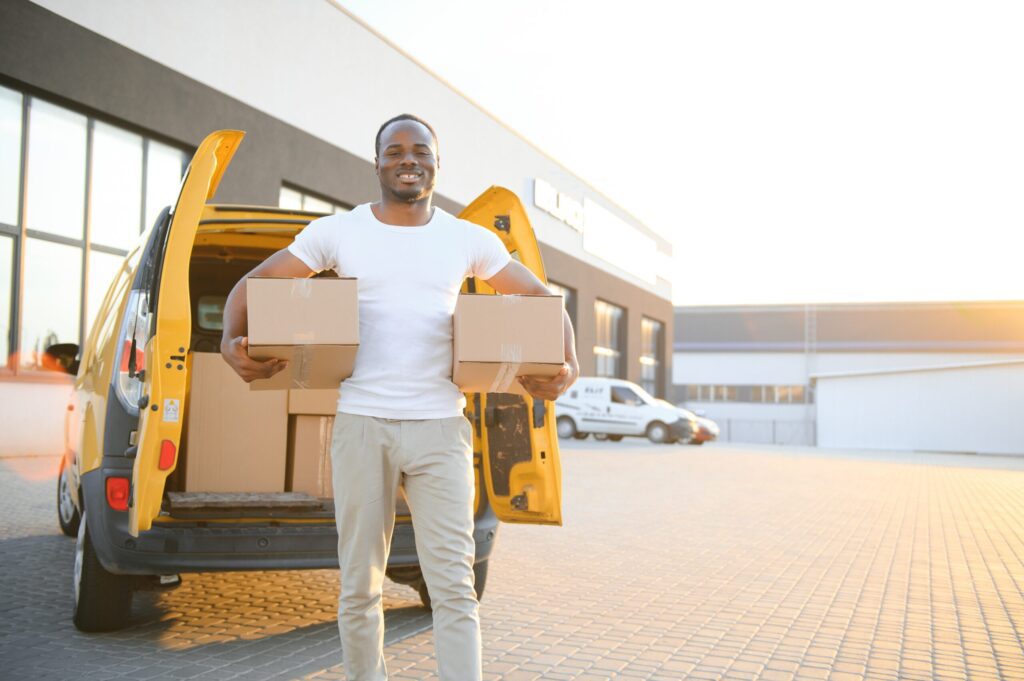 Commercial Moving Services in Philadelphia, PA Portrait of a young African American package delivery man near a car with boxes.